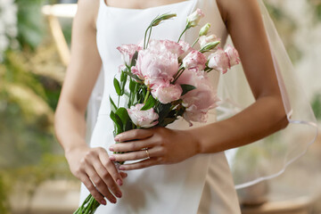 Closeup of young bride wearing wedding dress and holding delicate flower bouquet in pink tones, copy space