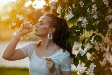 trendy 40 years old woman in white shirt using nasal spray