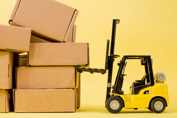 Forklift truck raises cardboard boxes on a yellow background. Cargo sorting concept