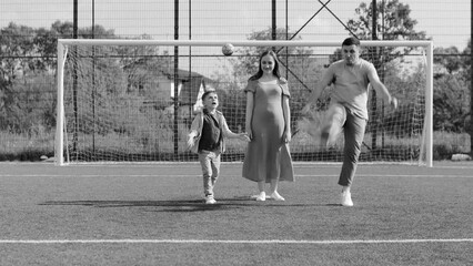 Expectant parents and here son are having a gender reveal party. Father and son are kicking a ball for find out the gender of the child.