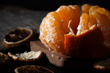 Close-up of half-peeled mandarin orange with separated segments, surrounded by dried citrus slices.