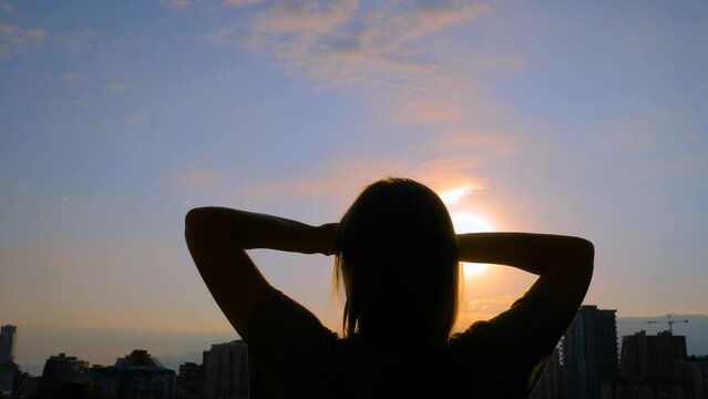 Back view: woman silhouette is stretching arms up against the sunrise sky with sun lens flare. Freedom, waking up, sport, morning and happiness concept