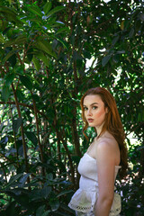 very beautiful freckled white woman with long red hair in a garden of green leaves