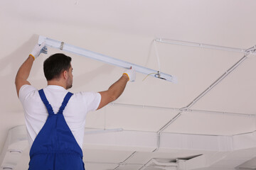 Ceiling light. Electrician installing led linear lamp indoors, back view. Space for text