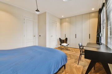 a bedroom with white closets and blue sheets on the bed in front of the bed is a black chair