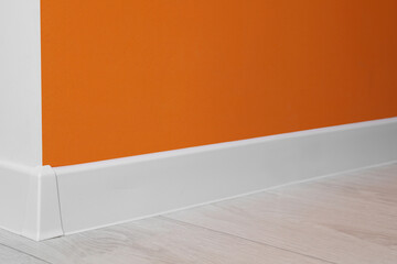 White plinth with connector on laminated floor near orange wall indoors