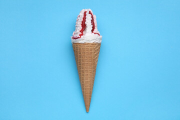 Delicious ice cream with raspberry jam in waffle cone on light blue background, top view
