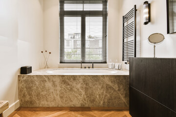 a modern bathroom with wood flooring and marble bathtub in the tub is surrounded by black shuttered windows