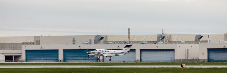petit avion en train de décoller sur une piste de décollage d'un petit aéroport avec des portes de hangar bleu - obrazy, fototapety, plakaty