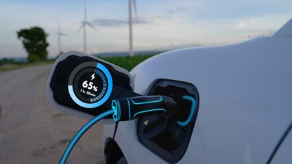 Electric car recharging energy from EV charging station display futuristic smart battery status hologram by EV charger plug cable in wind turbine farm. Alternative clean energy sustainability. Peruse