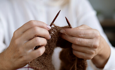 Woman's hands knitting brown wool yarn pattern. Closeup horizontal photo. Freelance creative...