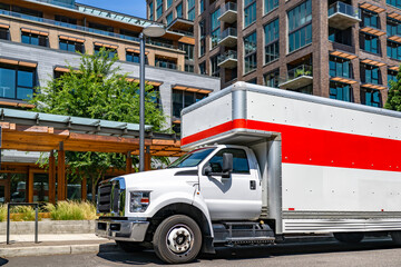 Middle duty rig semi truck with long box trailer with over roof compartment standing on the urban...