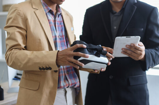 Close up shot of hands of two men in suit holding VR glasses headset and tablet, discussing about simulation and virtual reality project