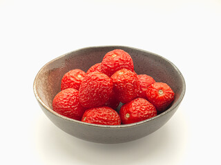 A pile of rotten tomatoes is on a bowl over a white background.