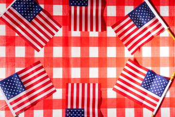 Obraz premium A top lay photo of a picnic table with a red and white checked tablecloth and little US flags forming a circle. The flags are arranged in a way that suggests patriotism and celebration.