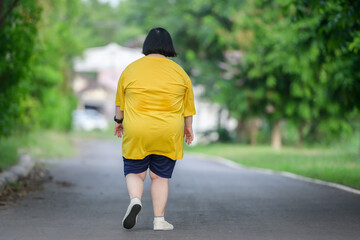 back view fat asian girl exercising By walking to burn fat and jogging slowly, fat woman walks for exercise in a natural park.