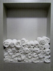 Rolled white soft hand towels on tile built in shelf in restroom