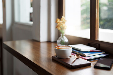 Close-up view, white coffee cup on wooden counter and smart phone, note book put on digital tablet by window, coffee break and relax after work in cafe