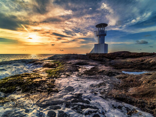 "Enchanting Coastal Serenity: Lighthouse, Rocks, and Evening Sun Overlooking the Sea Waves"