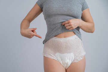A cropped portrait of a woman pointing at adult diapers on her. Urinary incontinence problem.