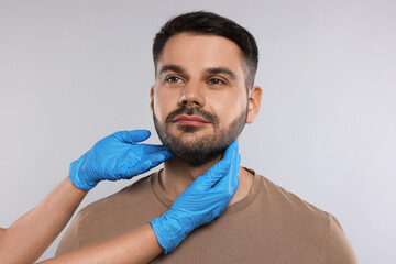 Endocrinologist examining thyroid gland of patient on light grey background, closeup
