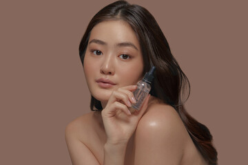 Charming asian ethnicity young model with a fresh smooth skin holding face moisturizer serum on a...