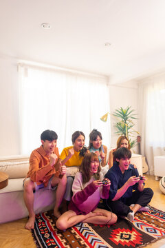 Group Of Young Asian Man And Woman Playing Video Games Together In Living Room At Home. Happy People Friends Enjoy And Fun Indoor Activity Lifestyle Spending Time Together On Holiday Vacation.