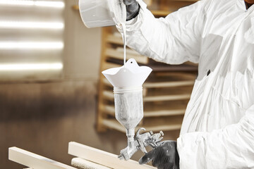 Man pours paint into the sprayer before painting the wood.