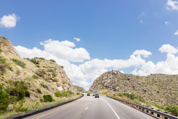 Fototapeta premium Beautiful summer landscape with highway among rocky mountains and blue sky with fluffy clouds on a summer day. Roadscape in New Mexico near Albuquerque, USA