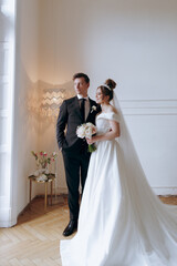 The first meeting of the groom in a black suit and the bride in a white wedding dress with a bouquet in the interior of a photo studio on a white and black background