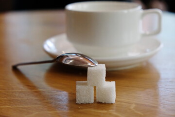 Cubes of refined sugar on the table with an empty white cup for coffee and tea.