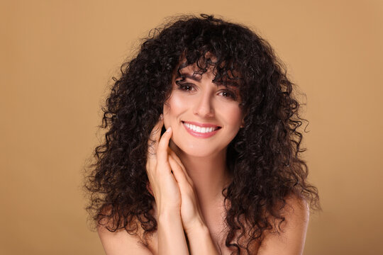 Beautiful young woman with long curly hair on beige background