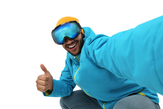 Smiling young man in ski goggles taking selfie and showing thumbs up on white background