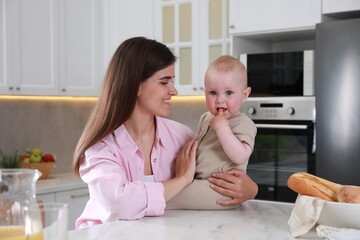 Happy young woman and her cute little baby spending time together in kitchen