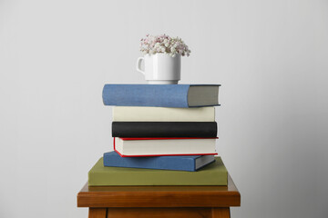 Hardcover books and cup with flowers on wooden stool near white wall