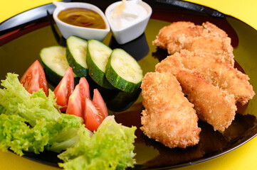 Chicken nuggets with cucumber, tomatoes and lettuce on a black plate, chicken nuggets on a yellow background.