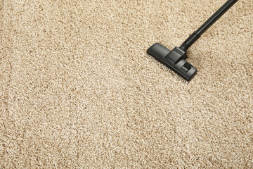 Hoovering beige carpet with modern vacuum cleaner, above view. Space for text