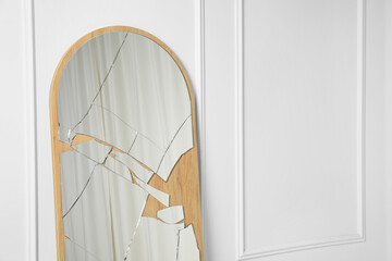 Fototapeta na wymiar Broken mirror with many cracks near white wall. Space for text