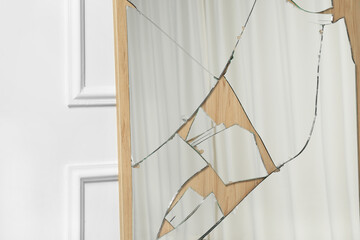 Broken mirror with many cracks near white wall, closeup