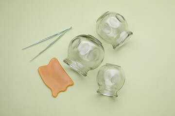 Glass cups, gua sha and tweezers on light olive background, flat lay. Cupping therapy