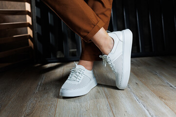 Slender female legs in pants close-up in white casual sneakers. Women's leather shoes.