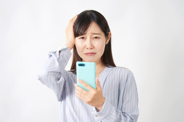 スマートフォンを持って頭を抱えるミドルエイジ女性　白背景