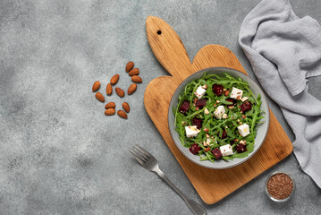 Bowl with beetroot salad with arugula and feta cheese. Gray concrete background. Top view, flat...