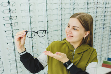 A young woman chooses glasses for vision correction. Ophthalmology shop with glasses to improve...