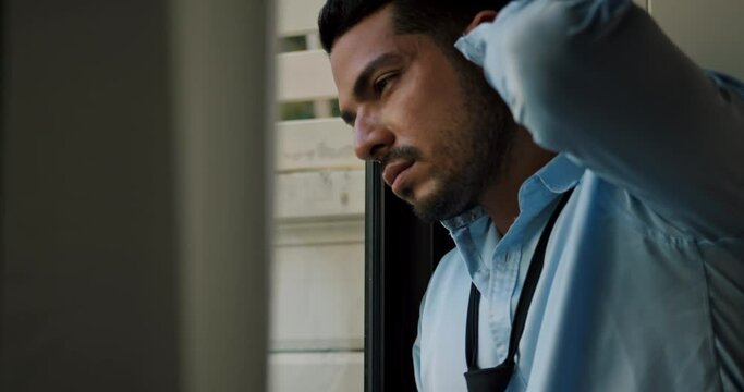 A young businessman is standing by the window depressed and stressed with problems in his life.