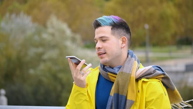 Young man wearing a yellow raincoat recording audio message on smart phone in the street in autumn.