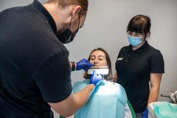 Fototapeta premium woman discusses teeth whitening with her dentist with a sample chart next to her teeth.