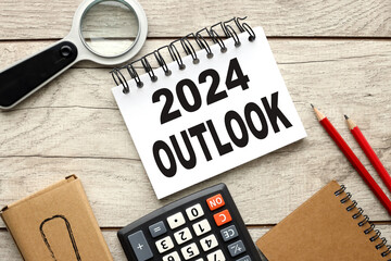 Economic outlook concept. Financial, business review or economic growth forecast for 2024. Turning OUTLOOK 2023 to 2024 t wooden background open notepad with text near calculator