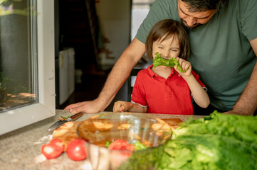 Son eating lettuce with father at home