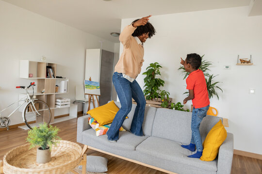 Cheerful mother and son dancing on sofa at home